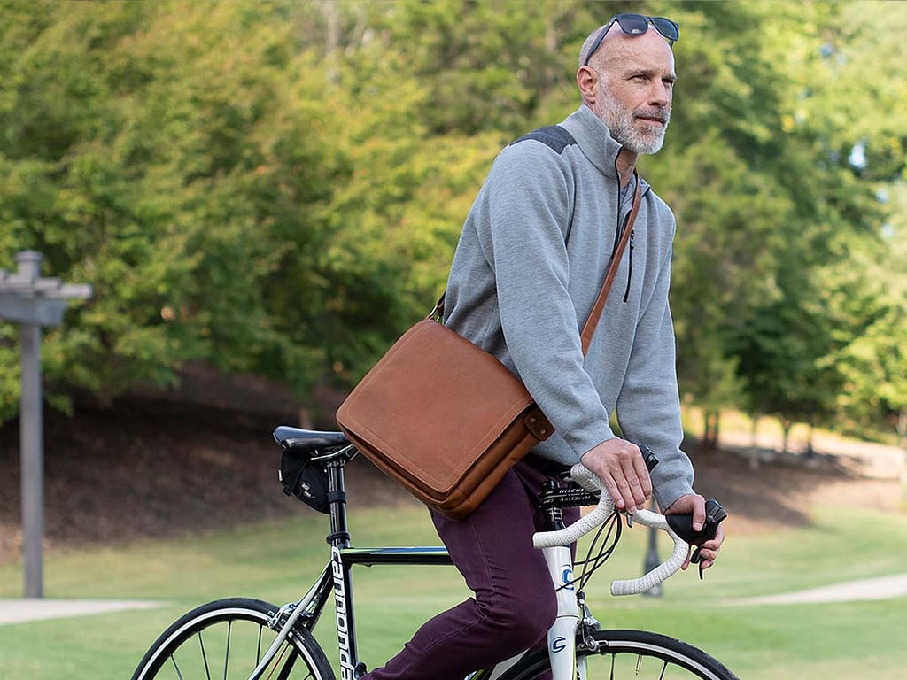 A man riding a bicycle while wearing a Sarge Leather messenger bag