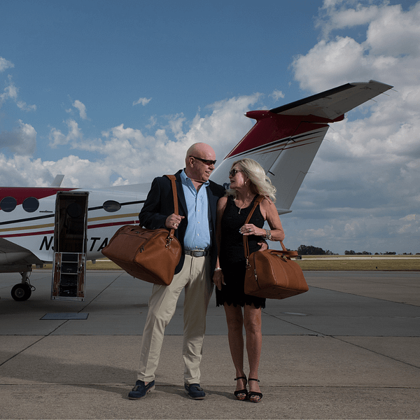 man and woman with leather duffle bags
